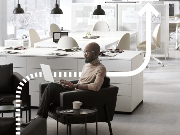 A person sits at a desk and works on a computer. We see a cellphone next to the person. The background shows more computers.