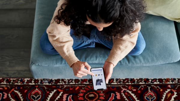 A person sitting on a blue sofa using a smartphone, with a red patterned rug on the floor below.