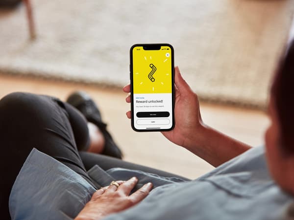 A person sitting on a sofa holding a phone and redeeming points with IKEA Family.