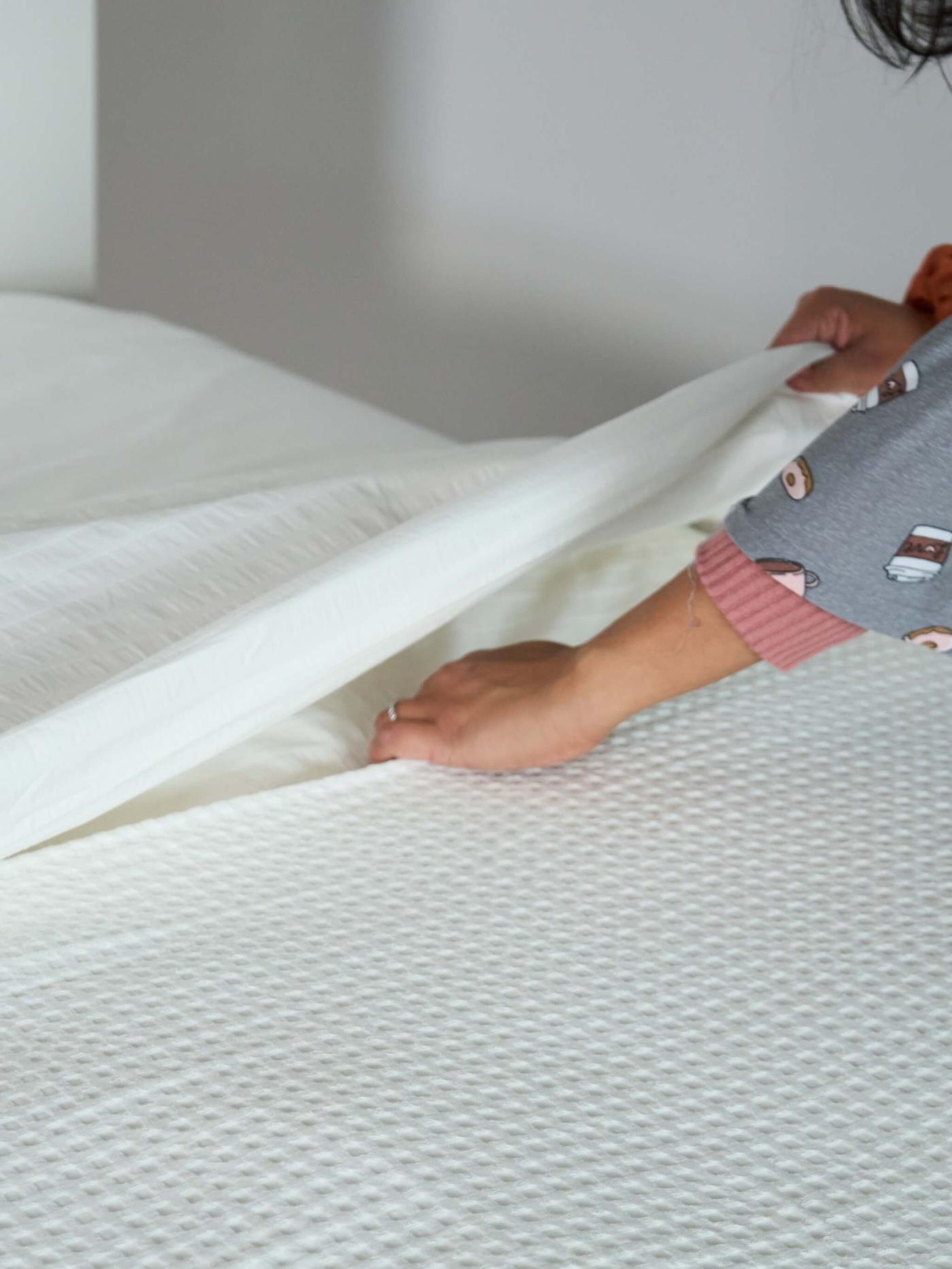 A person tucking a blanket under a white bedding while making a bed.