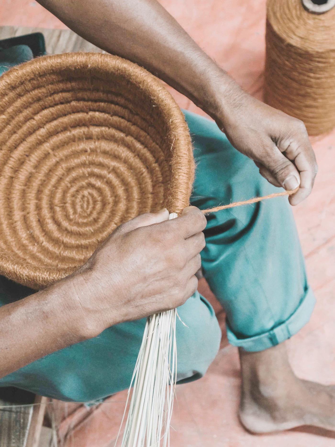 A person uses their hands to make a bowl from thick twine.