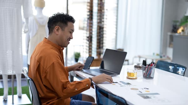 A person video calling on a laptop placed on four white BROR tables put together in the design office of a fashion company