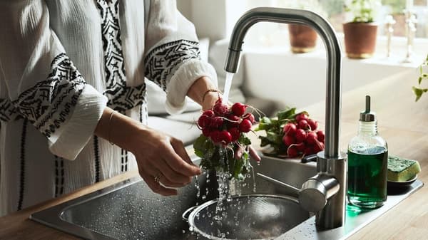 A person washing radish in a deep sink.