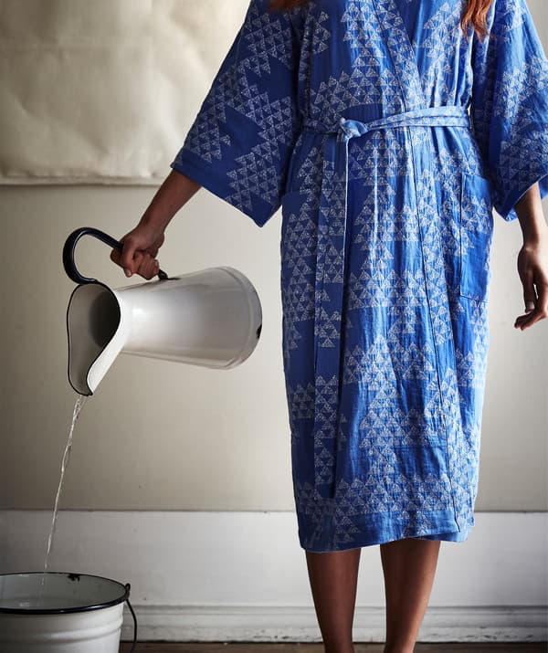 A person wearing a blue patterned kimono pouring water from a white jug into a bucket.