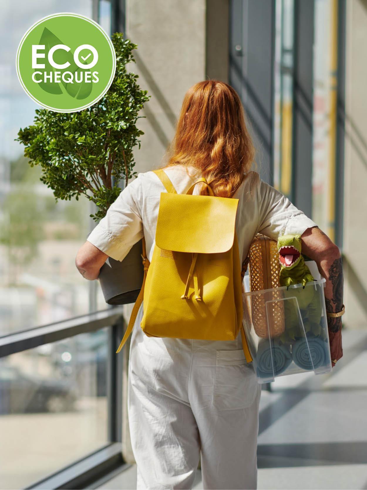 A person with long hair, dressed in white and carrying a yellow backpack, through a corridor while carrying a houseplant and a transparent container of groceries, with a green logo reading ‘ECO CHEQUES’ at the top left.