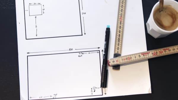 A pic with a pen, ruler, coffee and line drawings of a room design