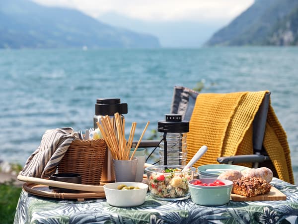 A picnic table covered in a jungle print table cloth, with various food containers filled with food