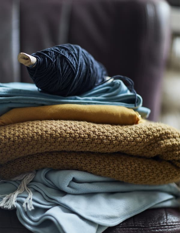 A pile of blue and yellow blankets and fabrics topped with a spool of wool.