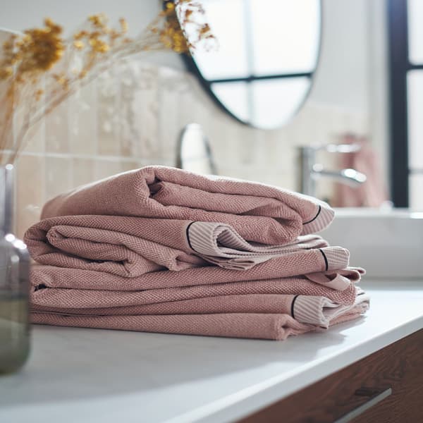 A pile of VIKFJÄRD hand towels in light pink stacked on a bathroom countertop