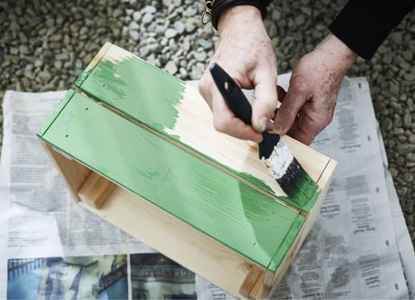 A pine box being painted with green paint.