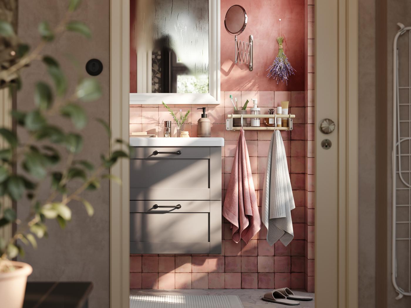 A pink bathroom with a gray ENHET cabinet with a white sink and a mirror above it and towels hanging on hooks next to it.