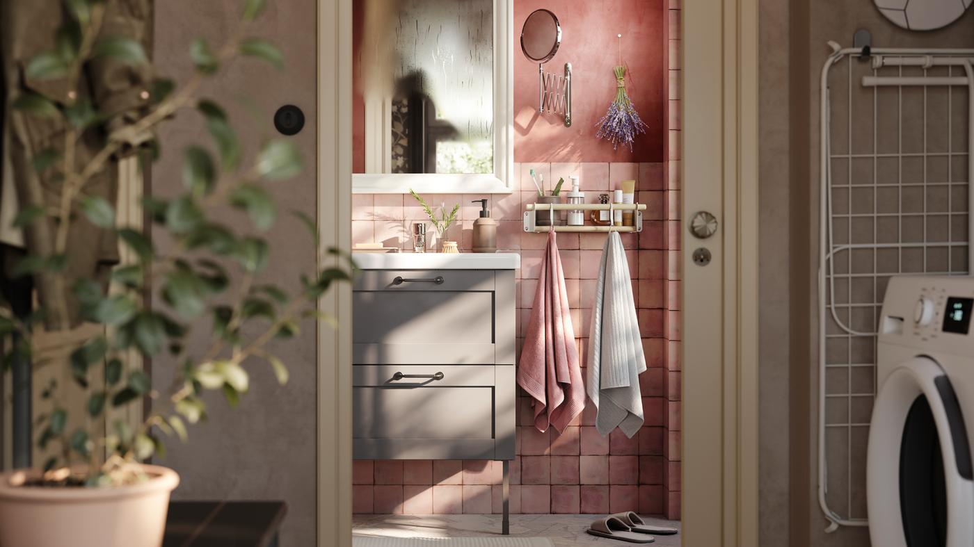 A pink-tiled bathroom with a grey ENHET cabinet on legs, a white mirror and two towels hanging from a rail with hooks.