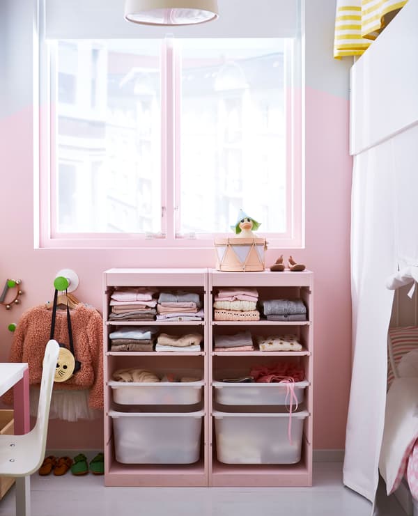 A pink wall with a window and a children’s TROFAST storage unit that’s painted pink and filled with clothes.