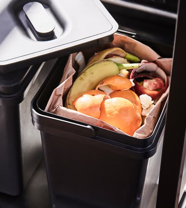 A plastic compost bin sits on the bottom shelf of a trolley.