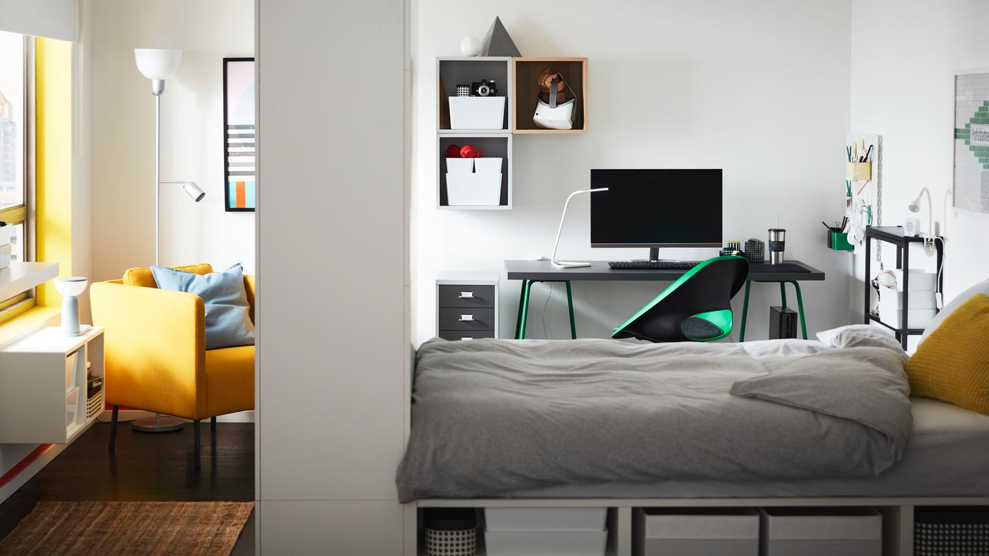 A PLATSA bed frame with storage in a room with an armchair and a green swivel chair in front of a desk with green trestles.