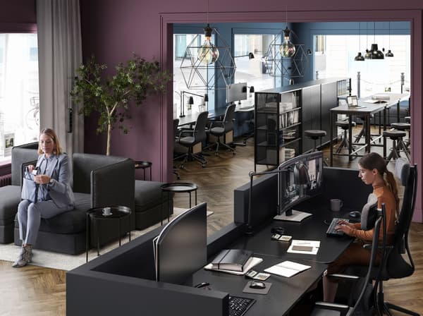 A plum-coloured reception area with a woman sat on black VALLENTUNA seating and another woman behind the black welcome desk.