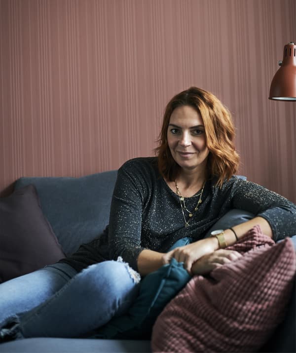 A portrait of Amélie sitting on a grey sofa against a red wall.