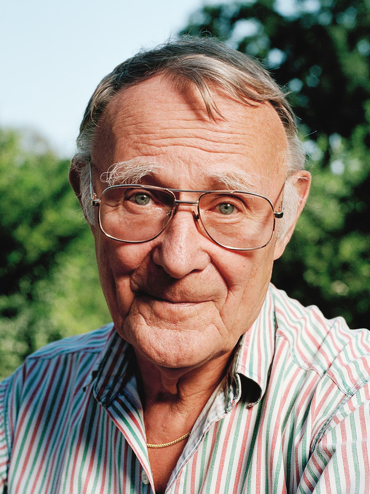 A portrait of IKEA founder Ingvar Kamprad, outdoors smiling while wearing a pink, white and green striped shirt.