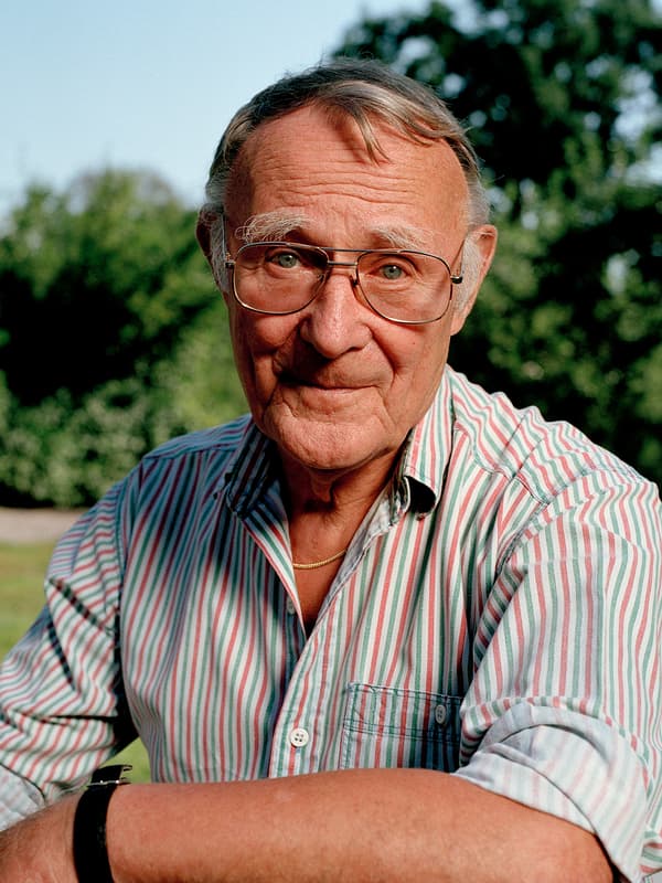 A portrait of IKEA founder Ingvar Kamprad, outdoors smiling while wearing a pink, white and green striped shirt.