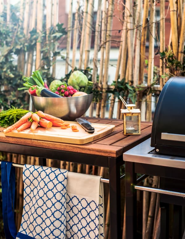 A prep station with a cutting board and lots of vegetables next to a grill.