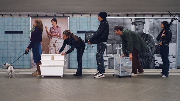 A queue of people waiting at the train station and each one is carrying a piece of furniture by hand