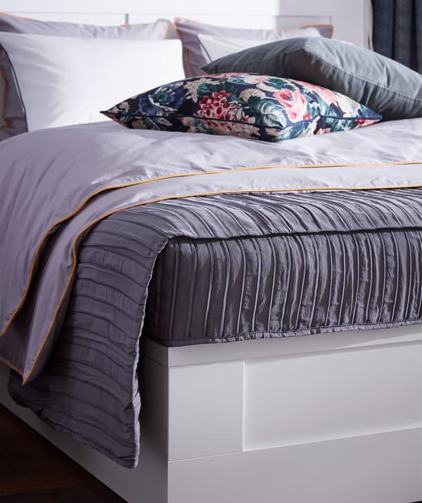A quilted, lilac IKEA VEKETÅG bedspread with a pleated surface laying on a bed.