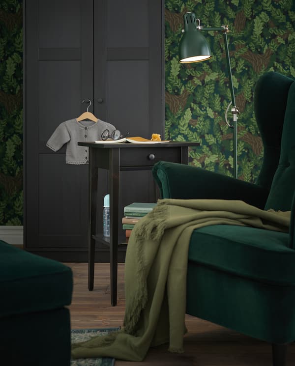 A reading corner with a green wing chair, a green floor lamp and a HEMNES bedside table used as a side table.