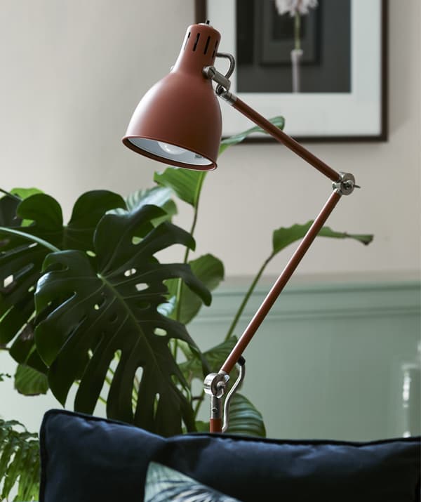 A red/brown floor lamp in a room with plants.