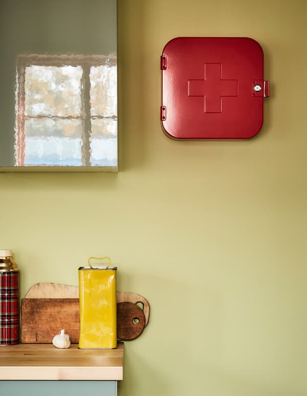 A red medicine cabinet sits on a kitchen wall next to a kitchen cabinet.