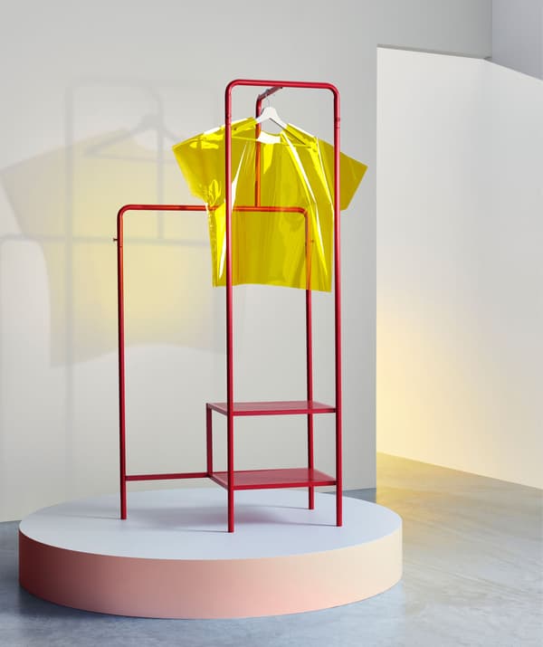 A red metal clothes rack on a podium with a yellow perspex t-shirt hanging from it.