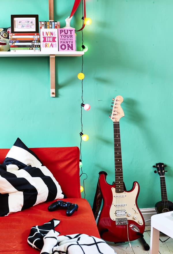A red sofa and guitar against a green wall.