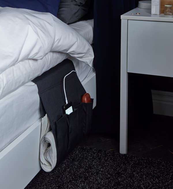 A remote control storage pocket is repurposed to hang by the side of the bed and store a charging mobile phone.