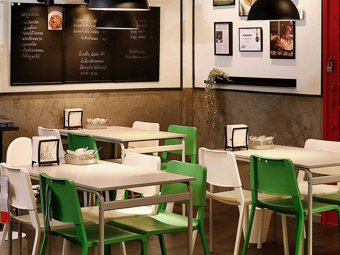 A restaurant setting featuring a blackboard and white tables with white and green chairs.