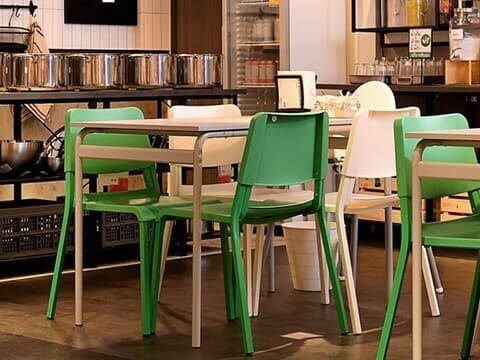 A restaurant setting featuring a blackboard and white tables with white and green chairs.