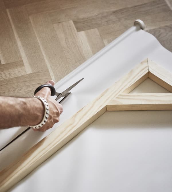 A roller blind is being cut to fit the wooden frame.