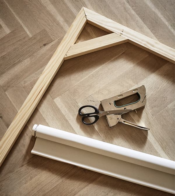 A roller blind, wooden frame, and staple gun lay on a floor.