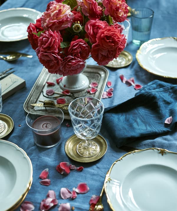A rose centrepiece on a blue tablecloth, with plates, candle and glass.