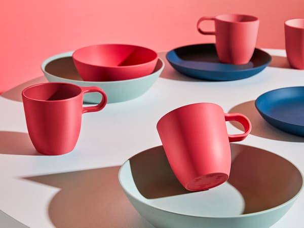 A round table filled with red, dark blue and pale green plates, bowls and cups from IKEA TALRIK series in PLA plastic.
