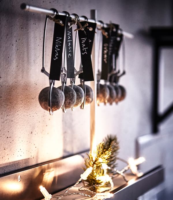 A row of IKEA IDEALISK tea infusers containing truffles and decorated with name tags hang in a kitchen.