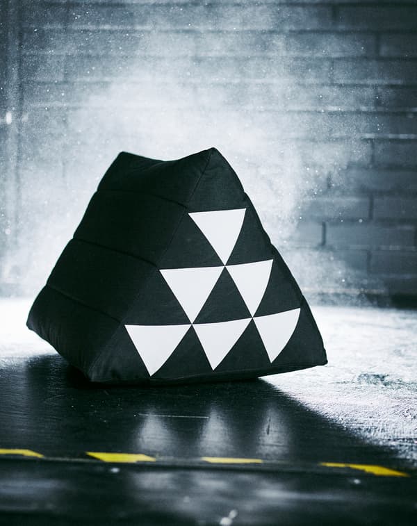 A SAMMANKOPPLA pillow stands in a dark room. The white triangle pattern on its side reflects the camera flash.