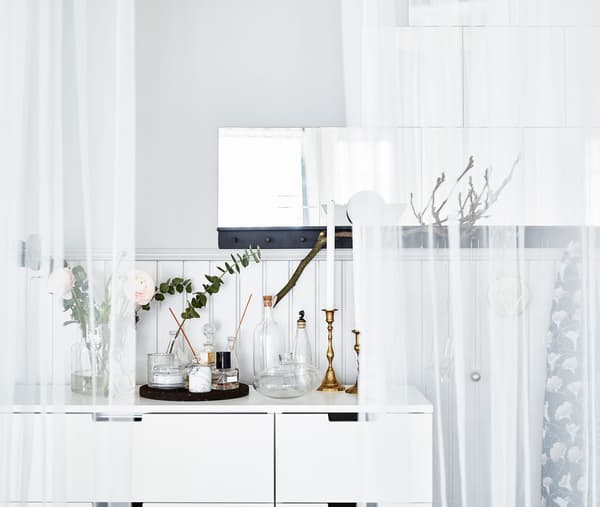 A scent station on top of a white dress unit with golden candlesticks and candles, flowers and perfumes.