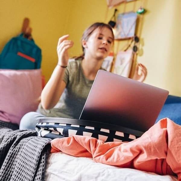 A schoolchild studies on her computer while sat on her bed, the laptop held steady by a BYLLAN laptop support.
