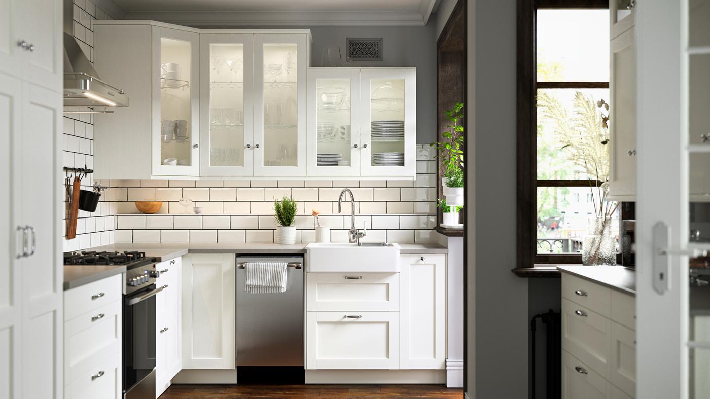 A SEKTION kitchen with white tiled walls and ENKÖPING fronts, plants on the windowsill and worktop, and white wall cabinets.