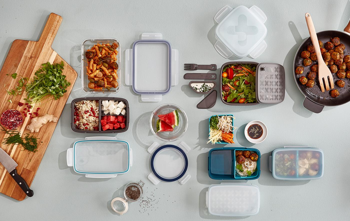 A selection of lunch boxes being prepared with lunch snacks, alongside a frying pan and chopping board.