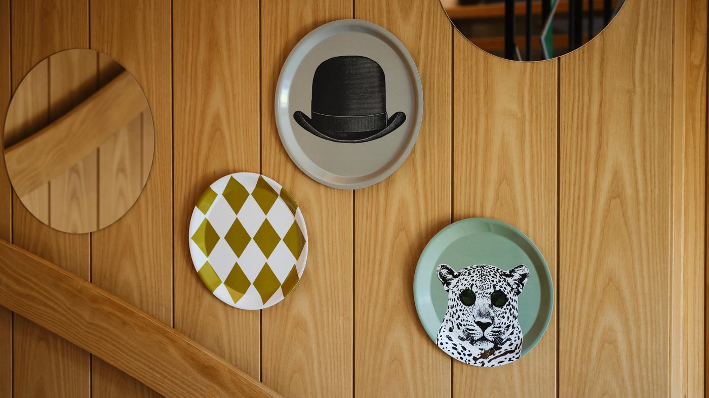 A set of three round GALLERISKOG wall decorations with whimsical prints are on a panelled wooden wall.