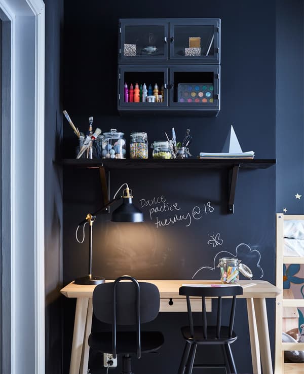 A shared desk for parent and child. Dark shelves are mounted on the dark wall above the wood desk and two work chairs.