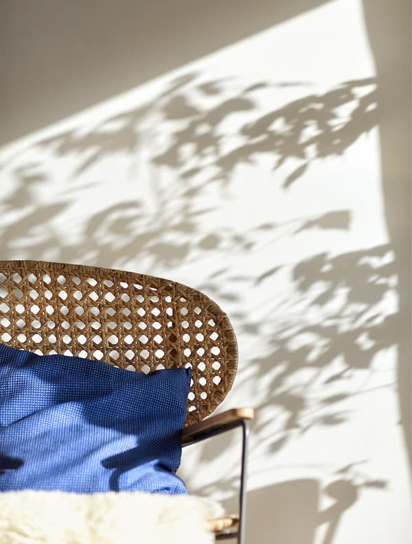A sheepskin and blue cushion on a wicker rocking chair.