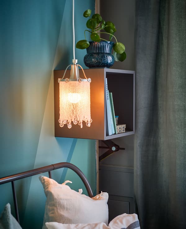 A shelf and a beaded lamp hang by a bed.