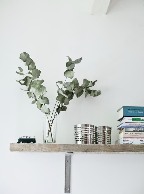 A shelf with a glass vase, decorative pots and books.