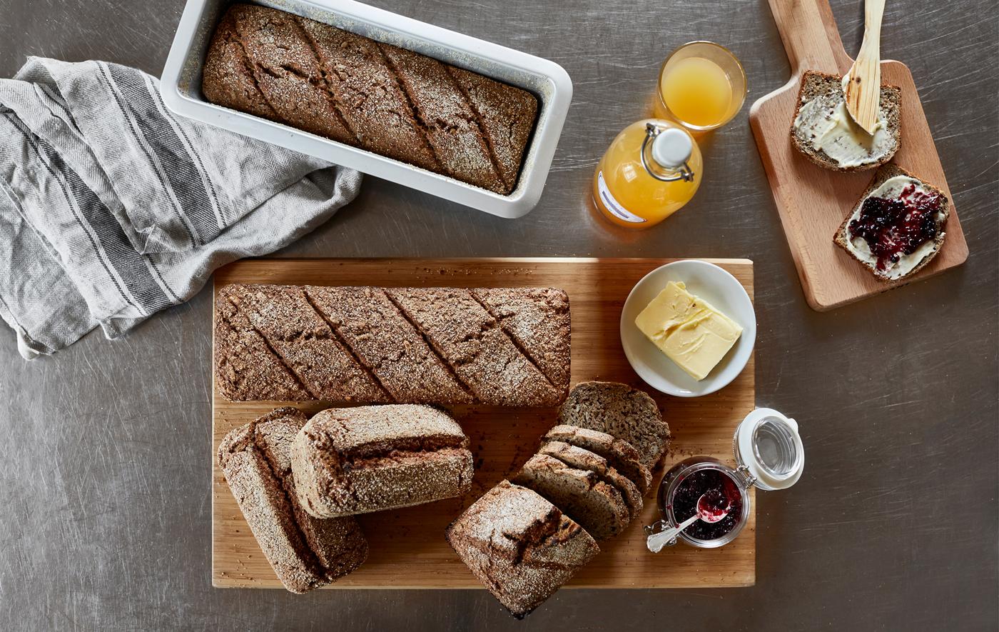 A shot from above of a table with prepared loaves of bread, butter, jam and orange juice.
